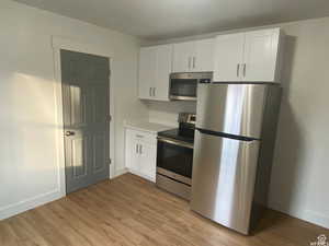 Kitchen featuring white cabinetry, stainless steel appliances, light countertops, and light wood finished floors