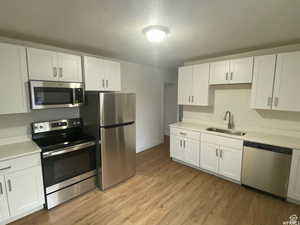 Kitchen featuring stainless steel appliances, white cabinets, light wood-style floors, and a textured ceiling