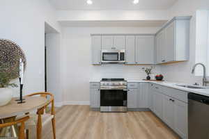 Kitchen with stainless steel appliances, gray cabinetry, light stone countertops, light wood finished floors, and recessed lighting