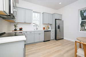 Kitchen with stainless steel appliances, light wood-type flooring, light stone countertops, gray cabinets, and recessed lighting