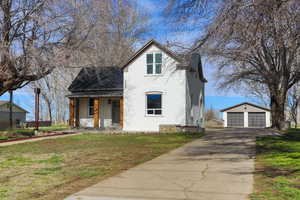 View of front of home featuring covered porch, a detached garage, an outdoor structure, stucco siding, and a front yard