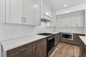 Kitchen featuring dual tone cabinets, gas stove, stainless steel microwave, backsplash, and light wood finished floors