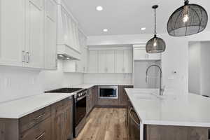 Kitchen featuring two tone cabinets, a center island with sink, stainless steel appliances, light stone counters, and light wood finished floors