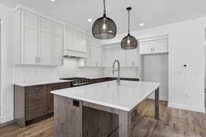 Kitchen featuring dual tone cabinets, dark wood-type flooring, an island with sink, hanging light fixtures, and stainless steel range with gas cooktop