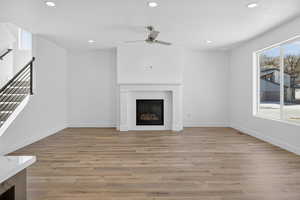 Unfurnished living room featuring recessed lighting, light wood-type flooring, a ceiling fan, and a glass covered fireplace