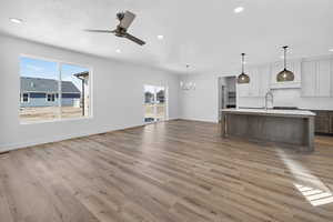 Kitchen featuring dual tone cabinets, open floor plan, a ceiling fan, an island with sink, and hanging lights