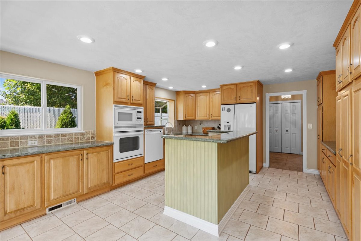 Kitchen featuring decorative backsplash, a kitchen island, white appliances, dark stone counters, and recessed lighting