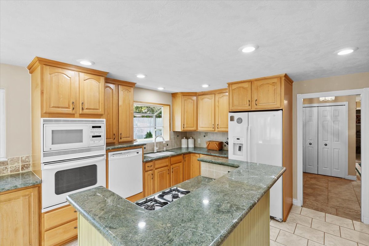 Kitchen featuring white appliances, a center island, backsplash, dark stone counters, and light tile patterned floors