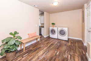 Laundry area with dark wood-style flooring, washing machine and dryer, a textured ceiling, and electric panel