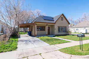 View of front facade with an attached carport, a shingled roof, stucco siding, roof mounted solar panels, and a front yard