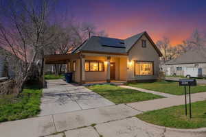 View of front of property featuring an attached carport, roof mounted solar panels, driveway, stucco siding, and a yard