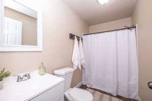 Full bathroom with vanity, a shower with shower curtain, light wood-style flooring, and a textured ceiling