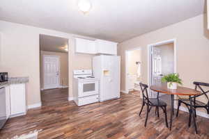 Kitchen with white cabinetry, white appliances, dark wood finished floors, light stone counters, and a textured ceiling