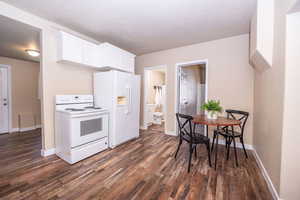 Kitchen with electric stove, dark wood-type flooring, white cabinets, and a textured ceiling