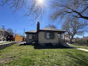 View of front of home with a chimney, stucco siding, a front yard, a shingled roof, and covered porch