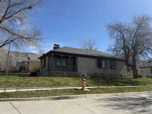 View of front of property with covered porch, a chimney, a front lawn, and roof with shingles