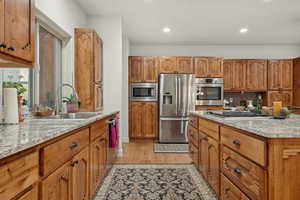 Kitchen featuring light stone countertops, wood finish cabinets, light wood finished floors, stainless steel appliances, and recessed lighting