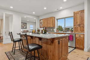 Kitchen with wood finish cabinetry, light stone countertops, light wood finished floors, tasteful backsplash, and a center island