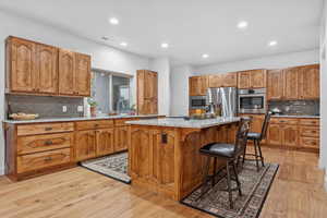 Kitchen with backsplash, wood finish cabinetry, light stone countertops, a kitchen island, and stainless steel appliances
