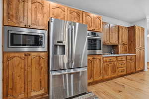Kitchen with stainless steel appliances, wood finish cabinets, light wood-style floors, and tasteful backsplash