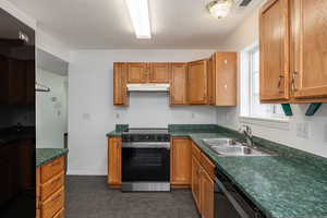 Kitchen with range with electric cooktop, dark countertops, wood finish cabinetry, and a textured ceiling