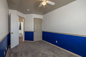 Unfurnished bedroom featuring dark carpet and ceiling fan