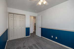 Unfurnished bedroom with dark colored carpet, a ceiling fan, and a closet