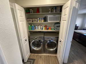 Laundry area featuring washer and clothes dryer, light wood-style flooring, and a textured wall