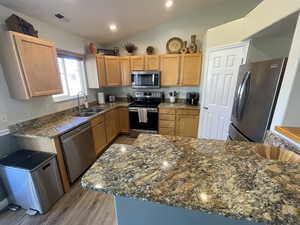 Kitchen featuring stainless steel appliances, wood finished floors, lofted ceiling, dark stone counters, and recessed lighting