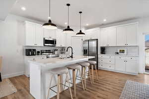 Kitchen featuring a breakfast bar, white cabinets, stainless steel appliances, and a kitchen island with sink