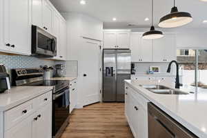 Kitchen with stainless steel appliances, white cabinetry, light wood-style floors, light stone counters, and pendant lighting
