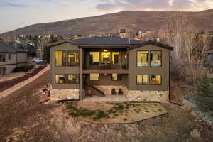 Rear view of property featuring board and batten siding, a patio, a balcony, a mountain view, and stone siding