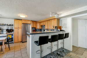 Kitchen with a kitchen bar, stainless steel appliances, a peninsula, a textured ceiling, and light tile patterned floors