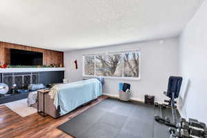 Bedroom featuring a brick fireplace, a textured ceiling, wood finished floors, and wood walls