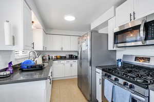 Kitchen featuring stainless steel appliances, decorative backsplash, white cabinets, and light tile patterned flooring