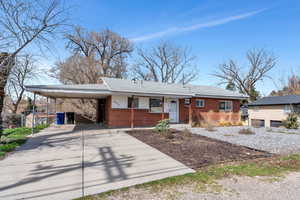 Ranch-style house with brick siding, a carport, driveway, a porch, and roof with shingles