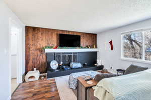 Bedroom with wooden walls, a brick fireplace, an accent wall, wood finished floors, and a textured ceiling