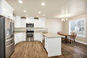 Kitchen featuring stainless steel appliances, a peninsula, white cabinetry, and light stone counters