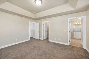 Unfurnished bedroom with a raised ceiling, carpet flooring, and ensuite bathroom