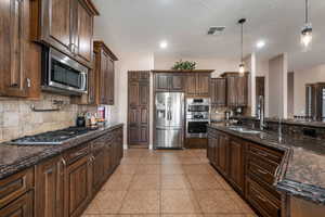 Kitchen with dark stone counters, dark wood finish cabinetry, stainless steel appliances, and a textured ceiling