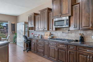 Kitchen featuring stainless steel appliances, dark wood finish cabinetry, dark stone countertops, and decorative backsplash