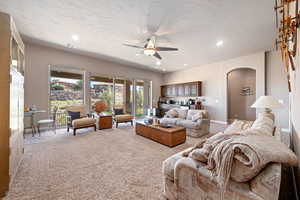 Living area with ceiling fan, light carpet, arched walkways, recessed lighting, and a textured ceiling