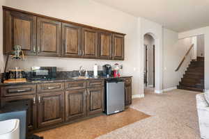 Kitchen featuring dark wood finish cabinets, arched walkways, stainless steel refrigerator, black microwave, and dark stone counters
