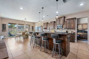 Kitchen with hanging light fixtures, a kitchen bar, dark stone counters, and a kitchen island with sink