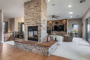 Living room with a stone fireplace, plenty of natural light, ceiling fan, tile patterned floors, and recessed lighting