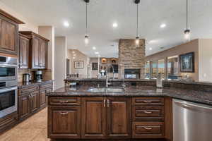 Kitchen featuring dark wood finish cabinetry, stainless steel appliances, dark stone counters, ceiling fan, and a stone fireplace