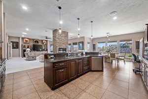 Kitchen featuring dark wood finish cabinets, decorative light fixtures, open floor plan, a fireplace, and dark stone countertops