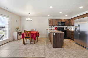 Kitchen featuring a peninsula, black appliances, dark wood finish cabinets, light countertops, and a chandelier
