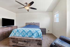 Carpeted bedroom with a ceiling fan and vaulted ceiling