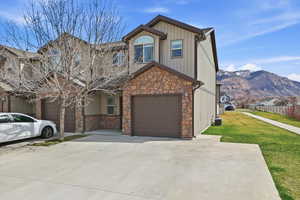 View of front of house featuring stone siding, a mountain view, concrete driveway, a front lawn, and an attached garage